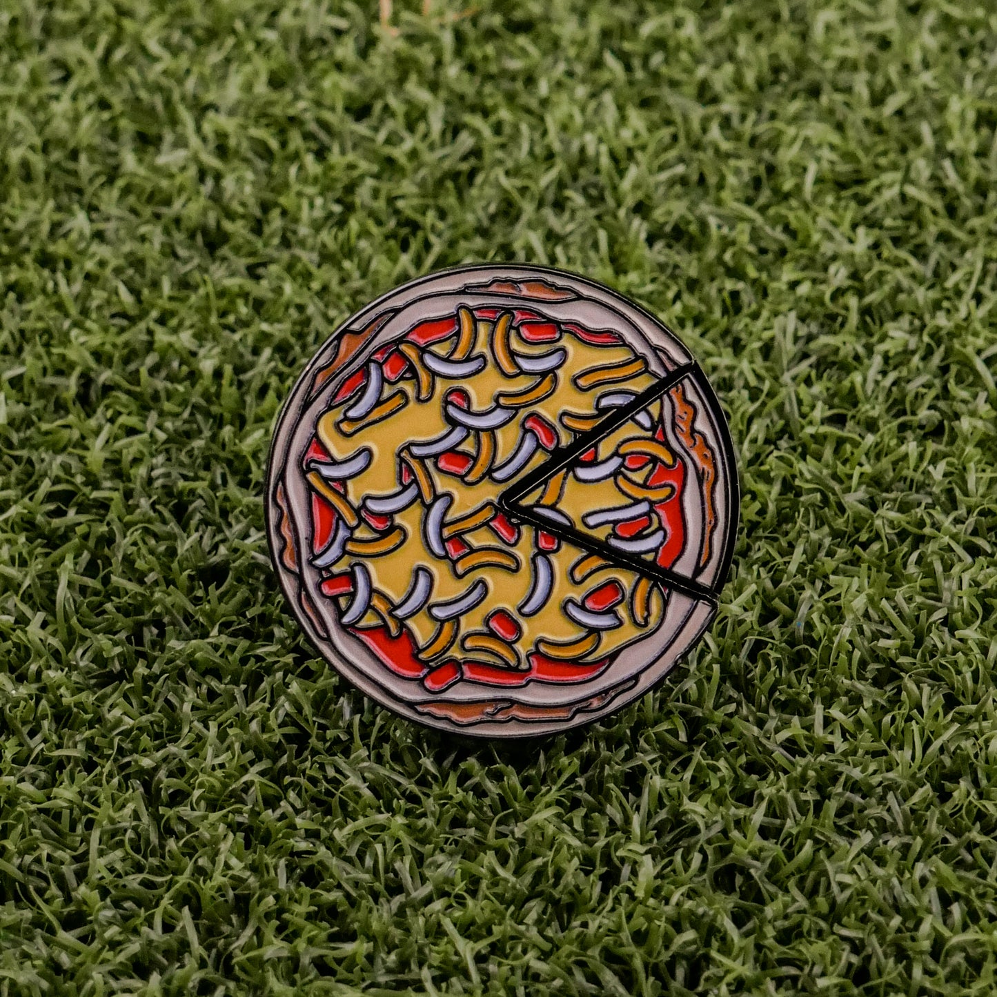 The Logie Joe's Golf Mexican Pizza "Slice" Premium Ball Marker, featuring colorful toppings and two removable slices, rests on green artificial grass.