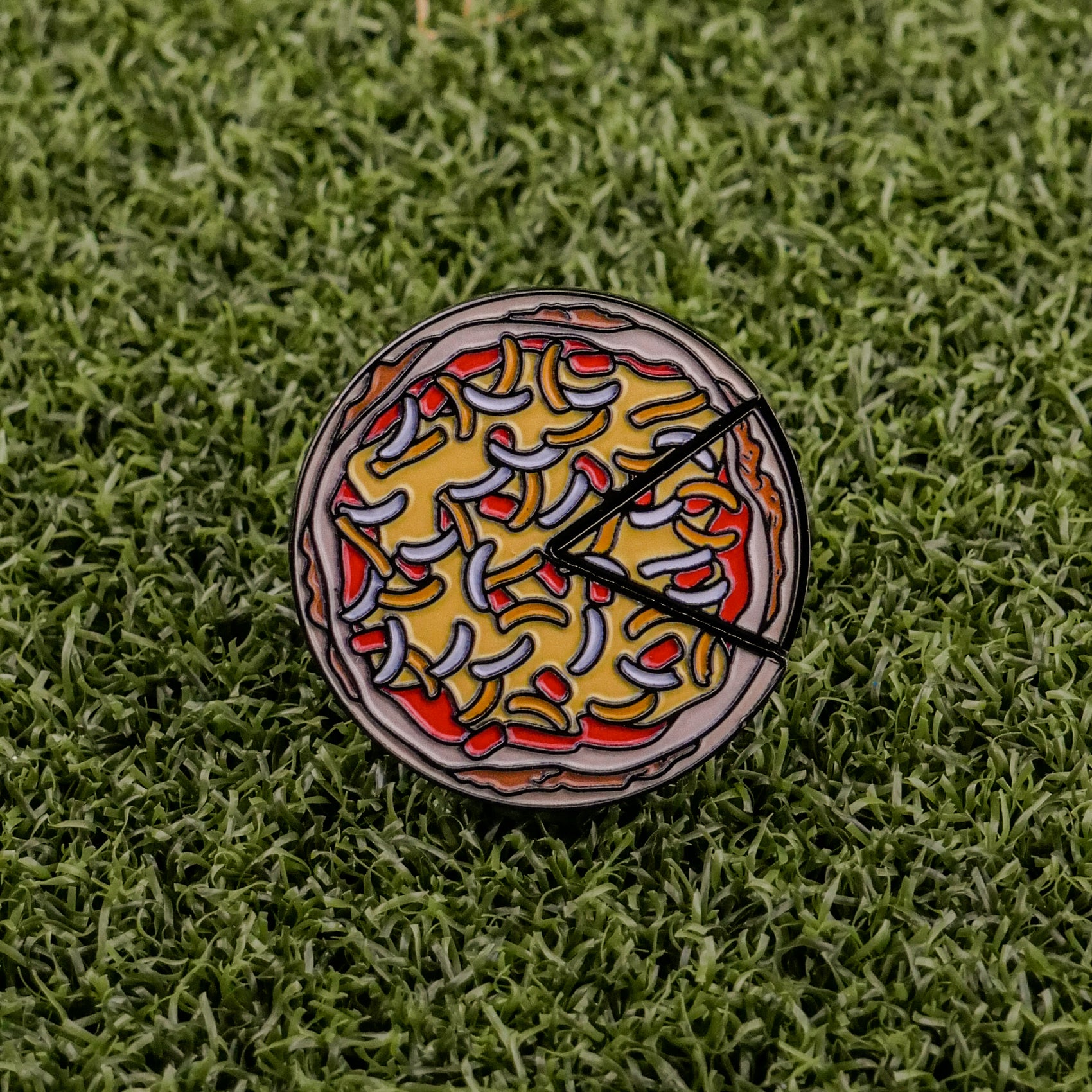 The Logie Joe's Golf Mexican Pizza "Slice" Premium Ball Marker, featuring colorful toppings and two removable slices, rests on green artificial grass.