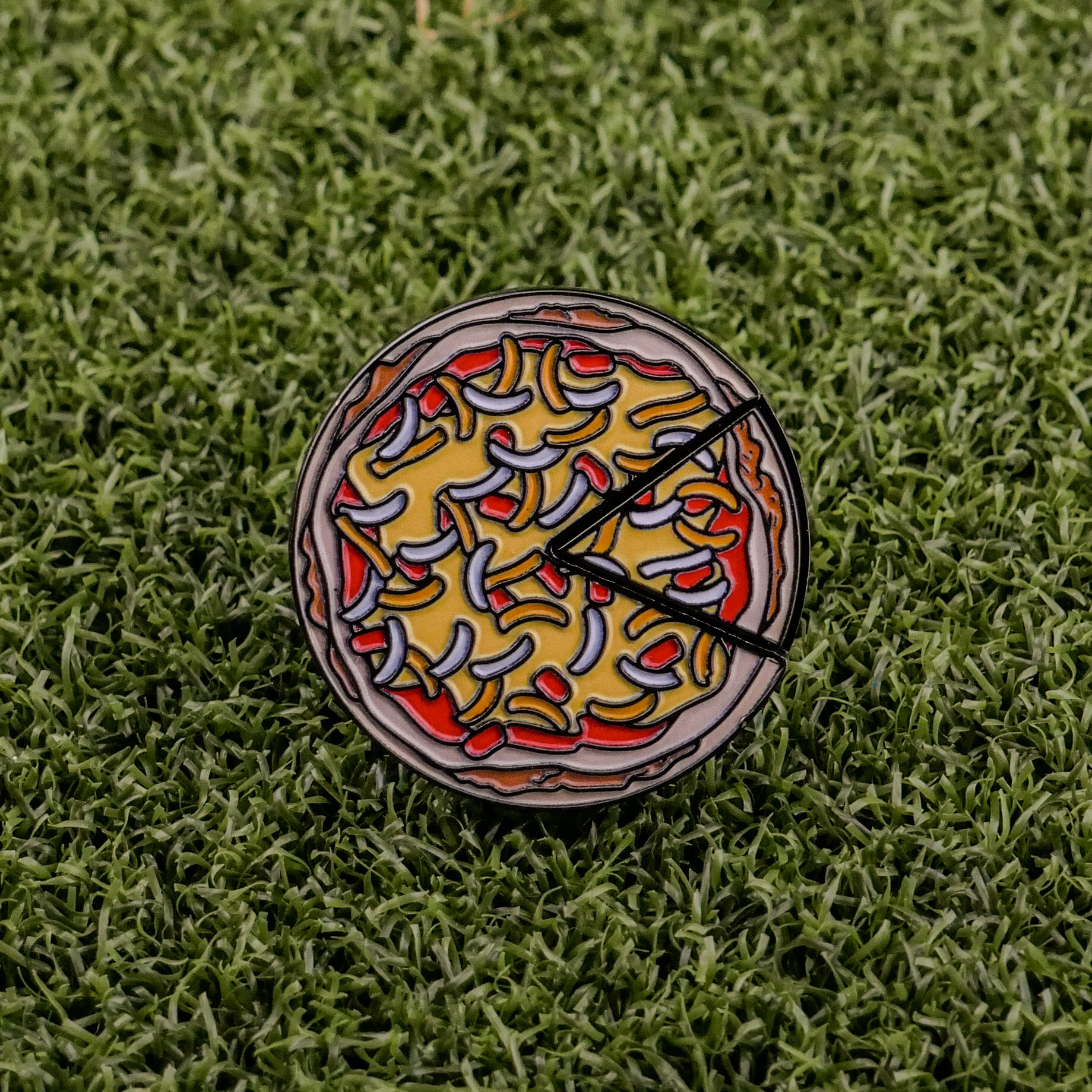 The Logie Joe's Golf Mexican Pizza "Slice" Premium Ball Marker, featuring colorful toppings and two removable slices, rests on green artificial grass.