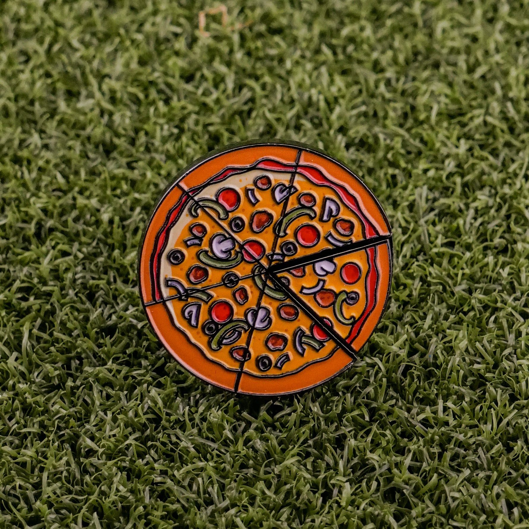 The Supreme Pizza "Slice" Premium Ball Marker by Logie Joe's Golf is a round enamel pin featuring pizza toppings and a removable slice, ideal as a quirky golf or poker chip ball marker on green grass surfaces.