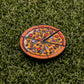 The Logie Joe's Golf Supreme Pizza "Slice" Premium Ball Marker, featuring black slice markings and removable slice detail, rests on artificial green grass.