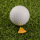 A white golf ball is on green artificial grass beside the Logie Joe's Golf Orange "Slice" Premium Ball Marker, a small, triangular orange marker designed to look like a removable slice.