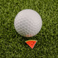 A white golf ball rests on artificial green grass beside Logie Joe's Golf Watermelon "Slice" Premium Ball Marker, a small triangular marker resembling a watermelon slice.