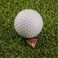 A white golf ball sits on Logie Joe's Golf Mexican Pizza "Slice" Premium Ball Marker, which displays a vibrant design atop bright green artificial turf.