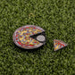 The Logie Joe's Golf Mexican Pizza "Slice" Premium Ball Marker, featuring a removable slice and vibrant toppings, adds a playful touch as it rests on green artificial grass.