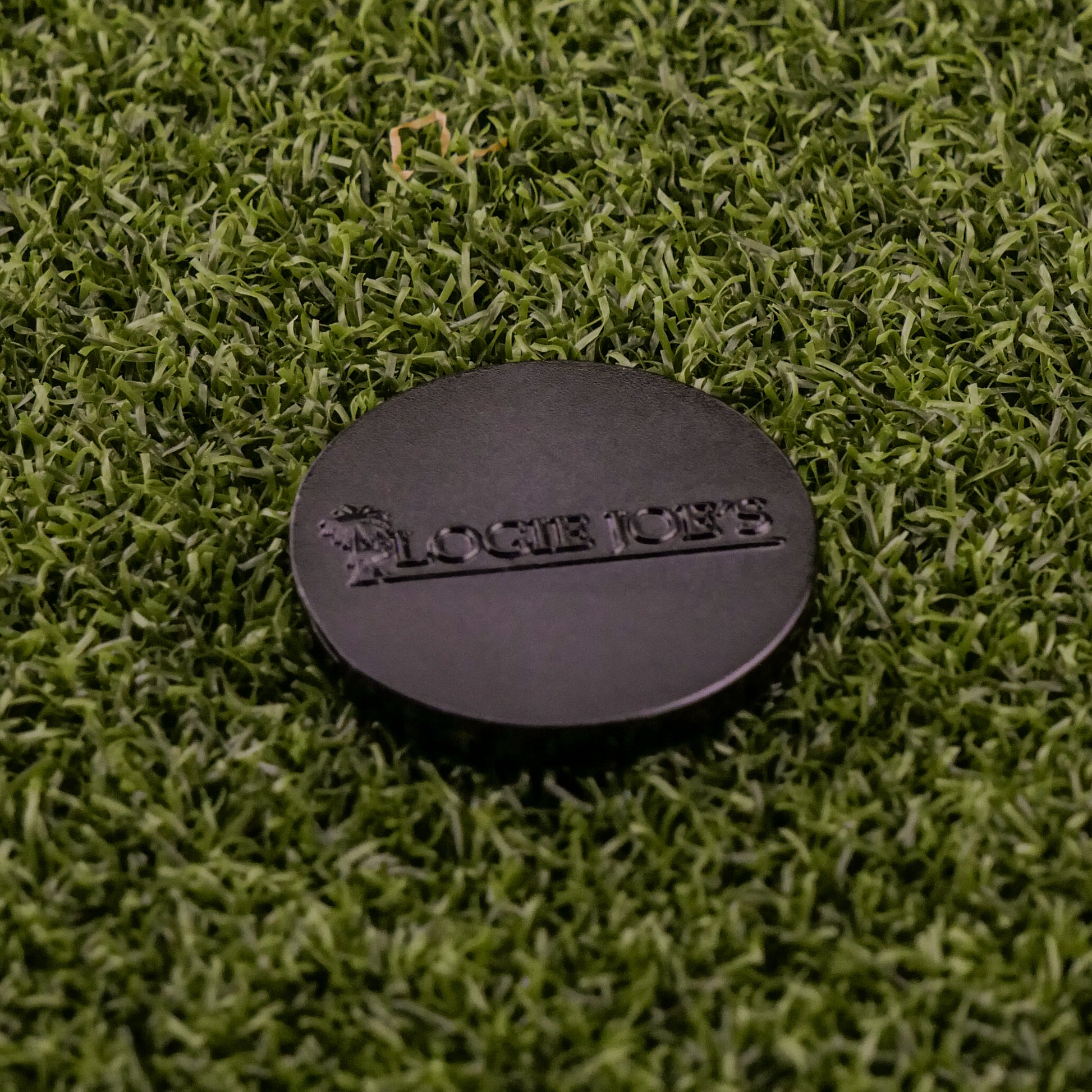 A Mexican Pizza "Slice" Premium Ball Marker by Logie Joe's Golf, shaped like a round disc, rests on artificial green grass.