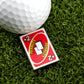 A close-up of a golf ball on artificial grass next to Logie Joe's Golf 2 Penalty Card - Red, one of the most humorous and unique premium golf ball markers you’ll find.
