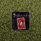The 2 Penalty Card - Red enamel pin by Logie Joe's Golf displays a red "+2 PENALTY" Uno card on a branded backing, set on green turf—ideal for golf fans seeking a fun, quirky alternative to standard ball markers.