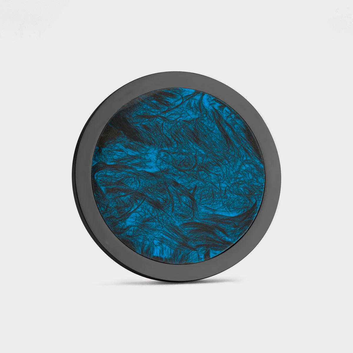 The Angler by Doubloon features a round design with a black rim and a blue and black marbled forged carbon fiber center, shown against a plain white background.