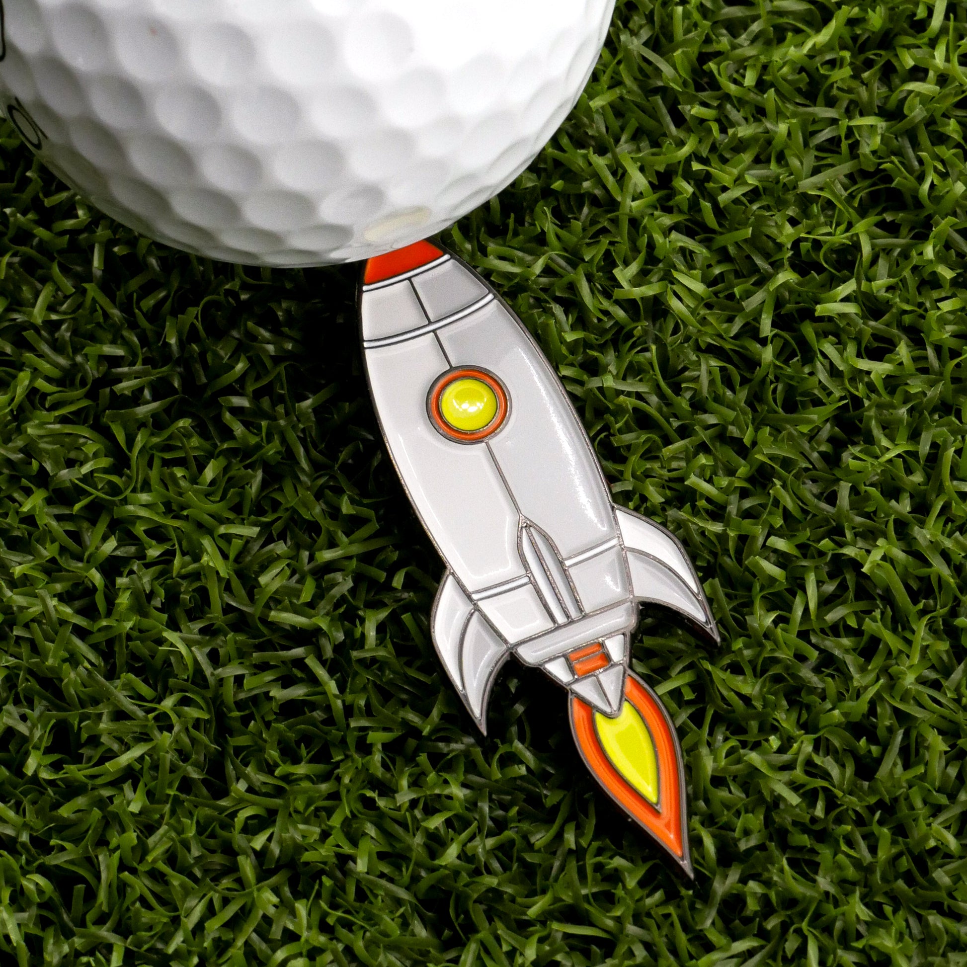 The Pocket Rocket Ball Marker by Ballmarkers.com sits on green grass beside a white golf ball, ready for your next shot.