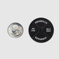 A U.S. quarter is placed next to the Guerrilla Golf 45lb Plate Ball Marker—a black, circular weight labeled "Guerrilla Standard"—shown on a plain white background, ideal for use as a heavy-duty gym ball marker or as a standard lifting accessory.