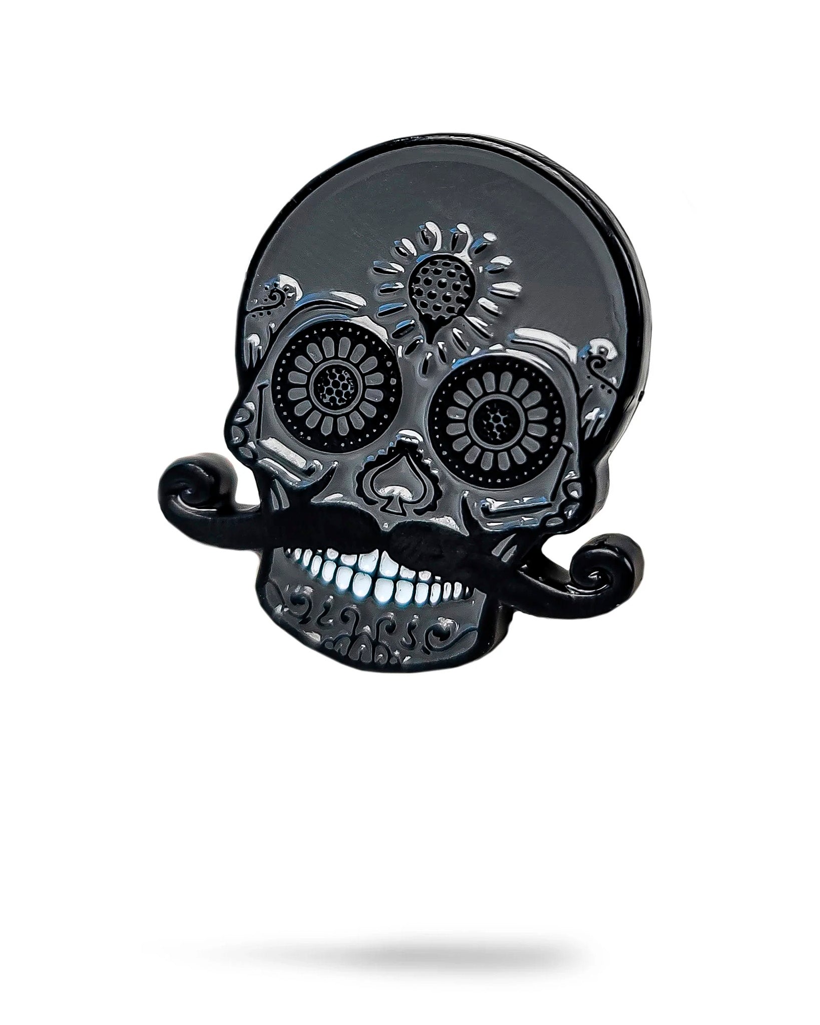 The Blackout Sugar Skull Ball Marker by Pins and Aces features decorative patterns, large eyes, and a curled mustache on a black stainless steel design. Perfect for use as a unique ball marker on any magnetic surface. White background with faint shadow shown.