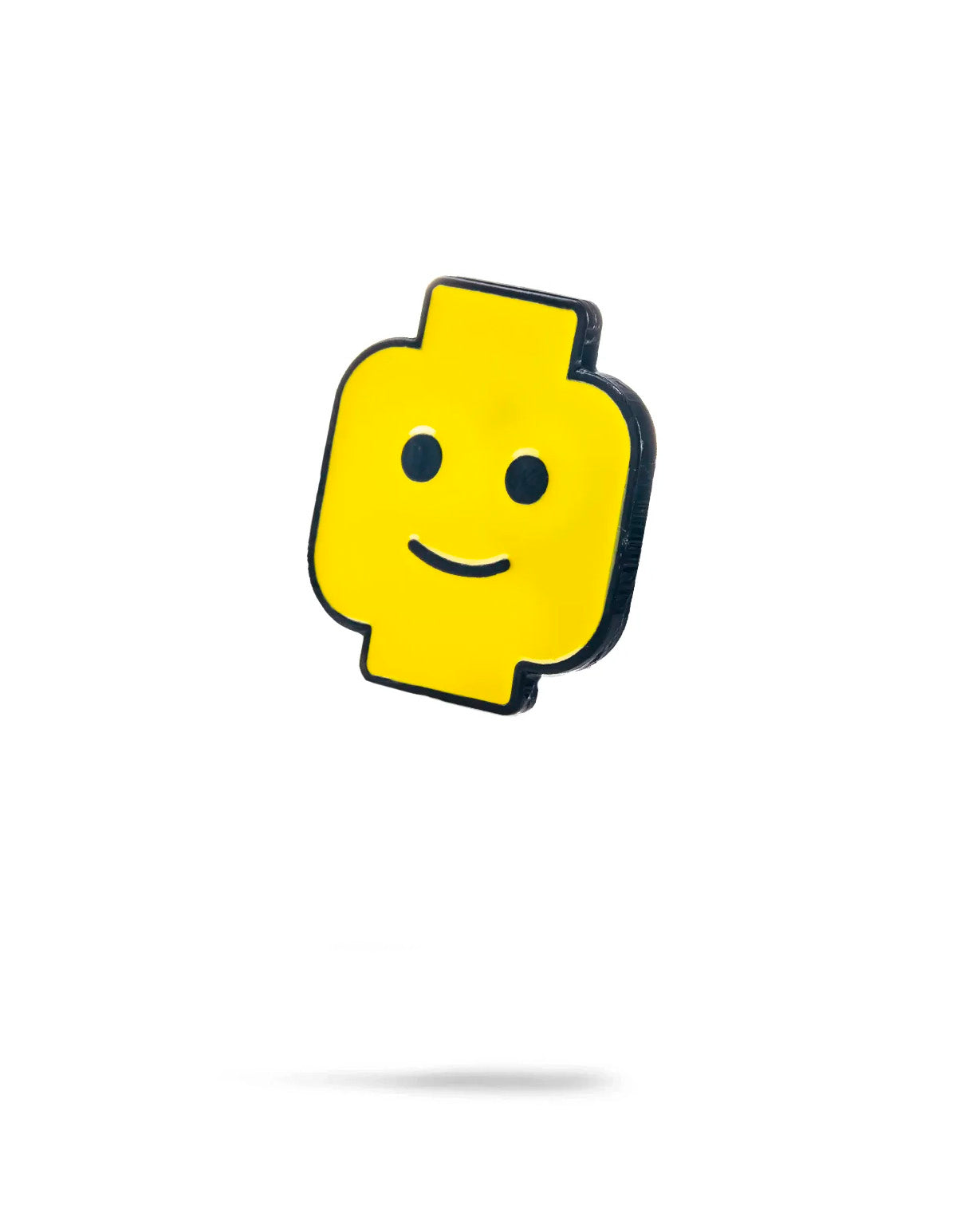 The Block Head Ball Marker by Pins and Aces features a yellow, stylized minifigure head with a simple black smile and eyes, resembling an enamel golf marker, shown against a plain white background with a soft shadow.