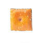 The Cheese Cracker Ball Marker by Pins and Aces features a golden-brown, slightly toasted cracker design with white spots, floating above a white background with a faint shadow—evoking the look of an enamel golf marker.