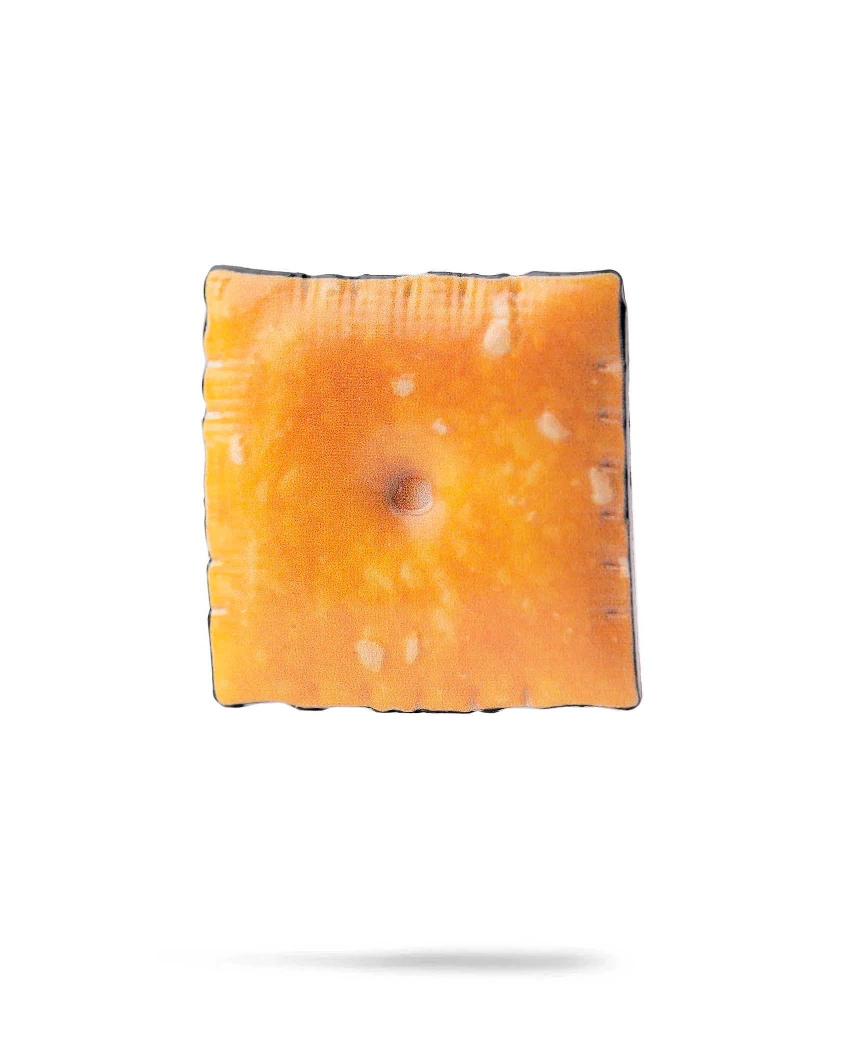 The Cheese Cracker Ball Marker by Pins and Aces features a golden-brown, slightly toasted cracker design with white spots, floating above a white background with a faint shadow—evoking the look of an enamel golf marker.