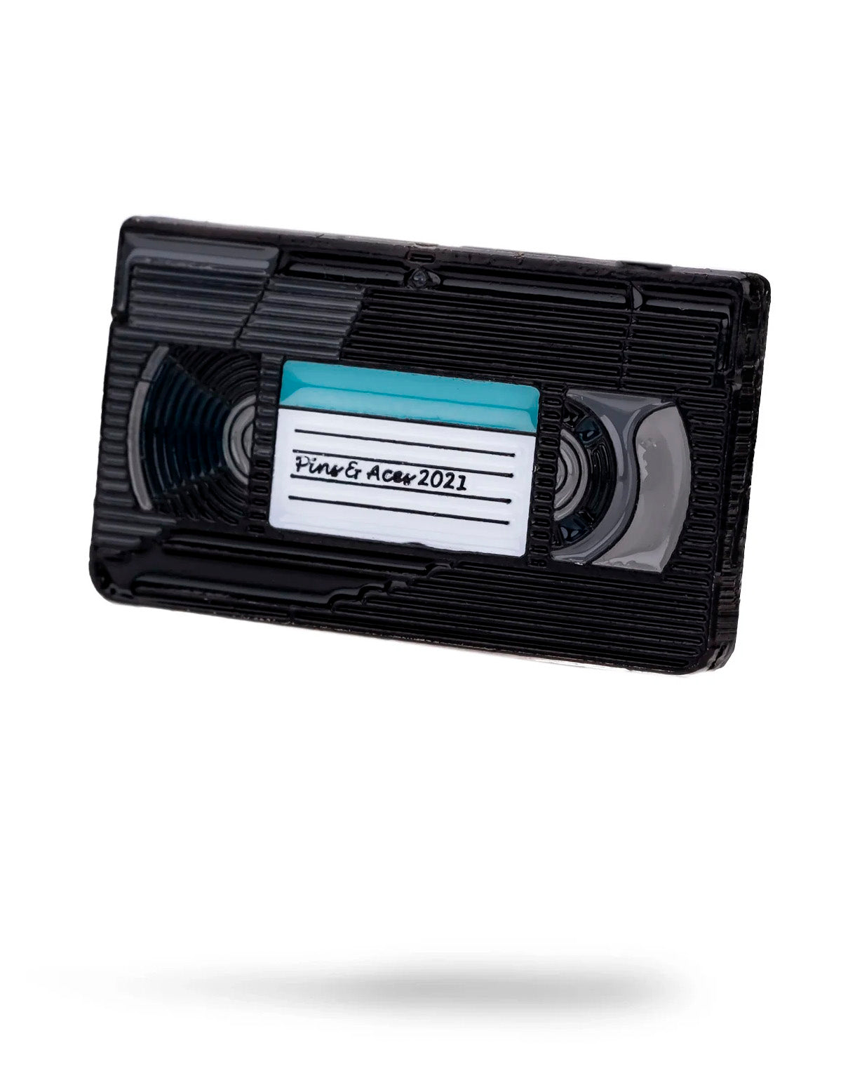 The VHS Ball Marker by Pins and Aces is shown—a black marker with a handwritten "Sing & Act 2021" label on a white background, casting a faint shadow. Its classic, simple design is reminiscent of enamel steel markers.