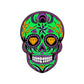 The Logie Joe's Golf Moon & Rest Sugar Skull Ball Marker features a vibrant Dia De Los Muertos-inspired design with green, purple, yellow, and black patterns, diamond-shaped eye sockets, and lightning bolts on the forehead.
