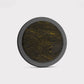 The Venom by Doubloon is a round object with a black outer rim and textured dark surface, highlighted by gold streaks and speckles. Made from forged Carbon Fiber and lightweight Titanium, it’s shown against a plain white background.