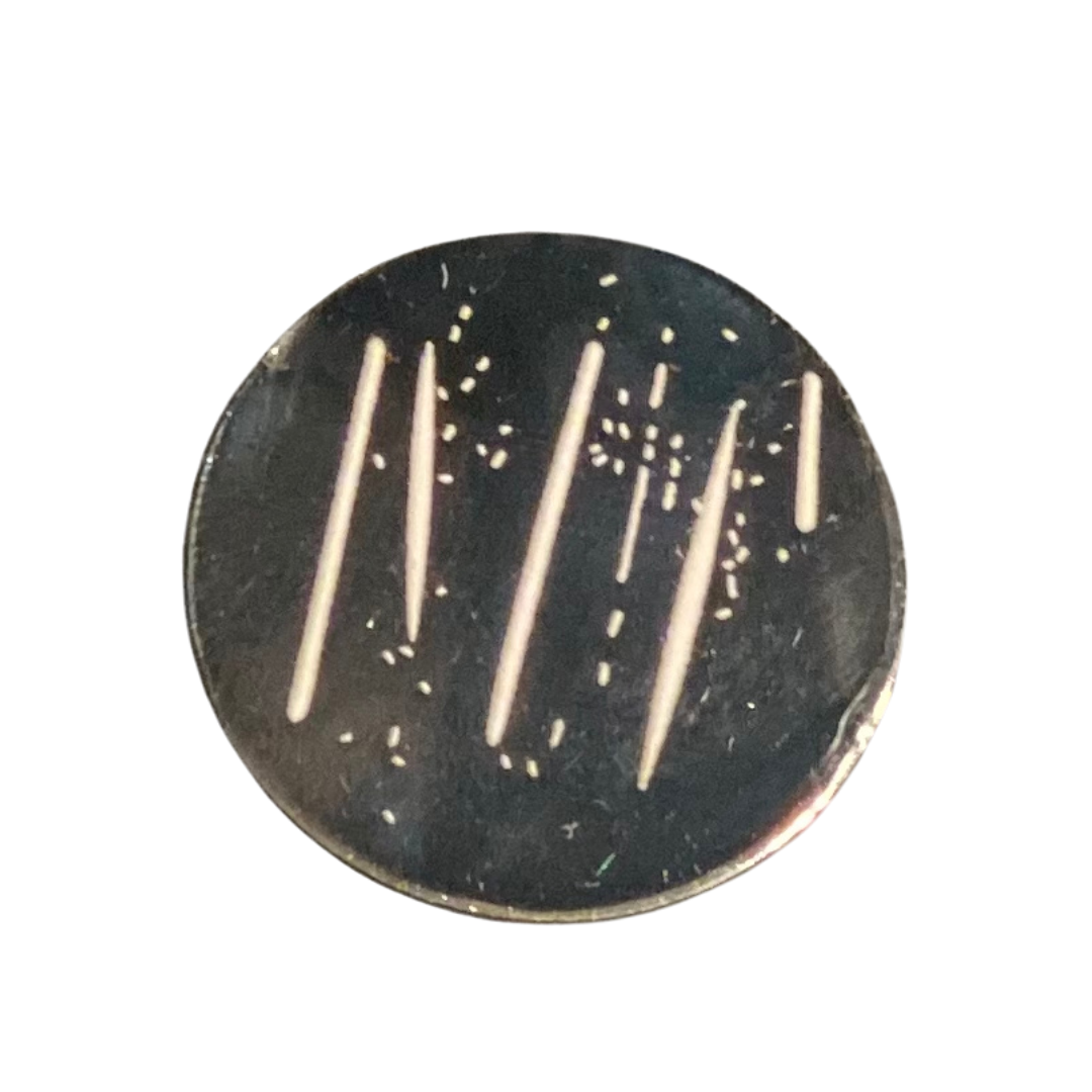 The TeeBumps Party Plate Ball Marker is a round, black marker about the size of a poker chip with several long, light streaks and small scattered dots on its surface, shown against a white background.
