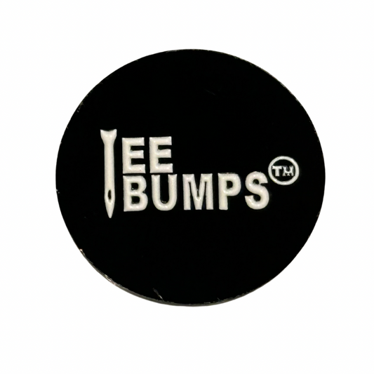 The Hawk Tuah 💦 Ball Marker by TeeBumps is a black, circular metal accessory with "EE BUMPS" in white, a nail design as the I, and TM symbol—ideal for marking your ball on the green.
