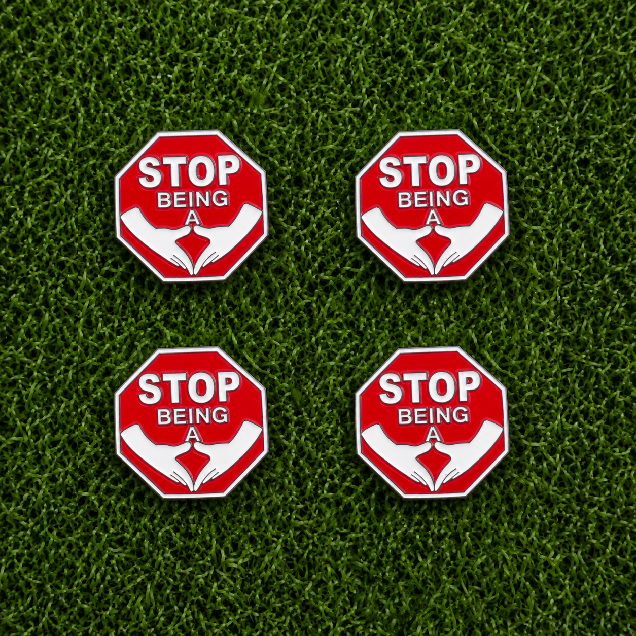 The Stop Being A P*%#! Ball Marker Bundle by Ballmarkers.com features four red octagonal markers with a hand gesture and bold message, arranged on green grass—a popular, humorous golf accessory inspired by the classic stop sign.