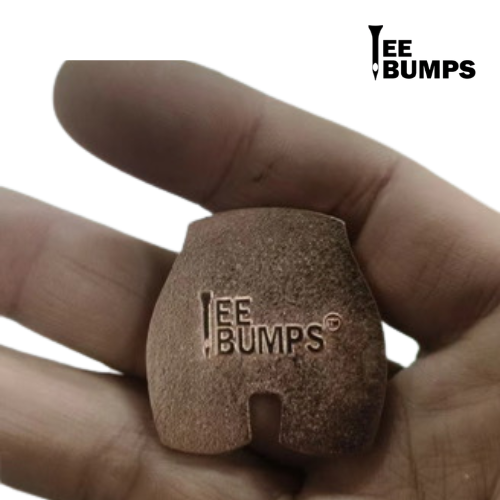A hand holds a small, brown, rounded Rack on the Back golf ball marker from TeeBumps, featuring a nail-shaped logo and "TeeBumps" text. The same branding appears in the image's top right corner.