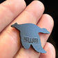 A close-up of a hand holding a Flying Mallard Ball Marker by Pins and Aces, shaped like a mallard and featuring glossy enamel paint with the brand name engraved on its back.