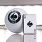 A premium golf accessory: the Pins and Aces Ace of Spades Ball Marker, shaped like the ace of spades, alongside a white golf ball with a black spade logo—both elegantly reflecting on a gleaming surface.