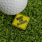 The Logie Joe's Golf Baby On Board Ball Marker, a funny yellow golf accessory, is shown on artificial grass beside a white golf ball.