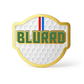 THE BLURRD PREMIUM BALL MARKER by BLURRD features a gold-edged, golf ball-textured design with bold green "BLURRD" lettering and a red, white, and blue stripe—an essential, stylish magnetic golf accessory.