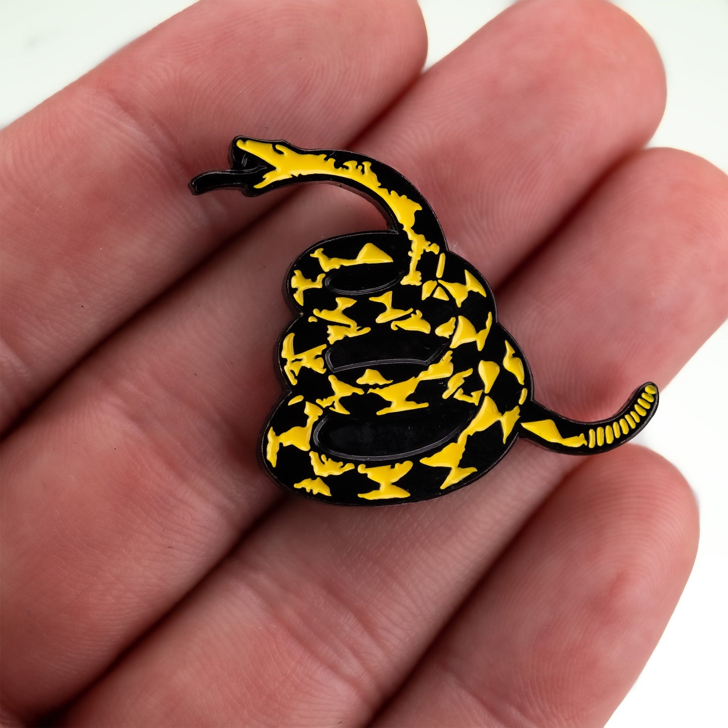 A hand holds the "Don't Tread on Me Ball Marker" by Pins and Aces, featuring a detailed yellow and black coiled snake with its tongue out against a sleek, stainless steel magnetic surface.