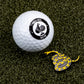 A Pins and Aces golf ball sits on artificial green turf next to the Don't Tread on Me Ball Marker, a yellow and black snake-shaped stainless steel marker.