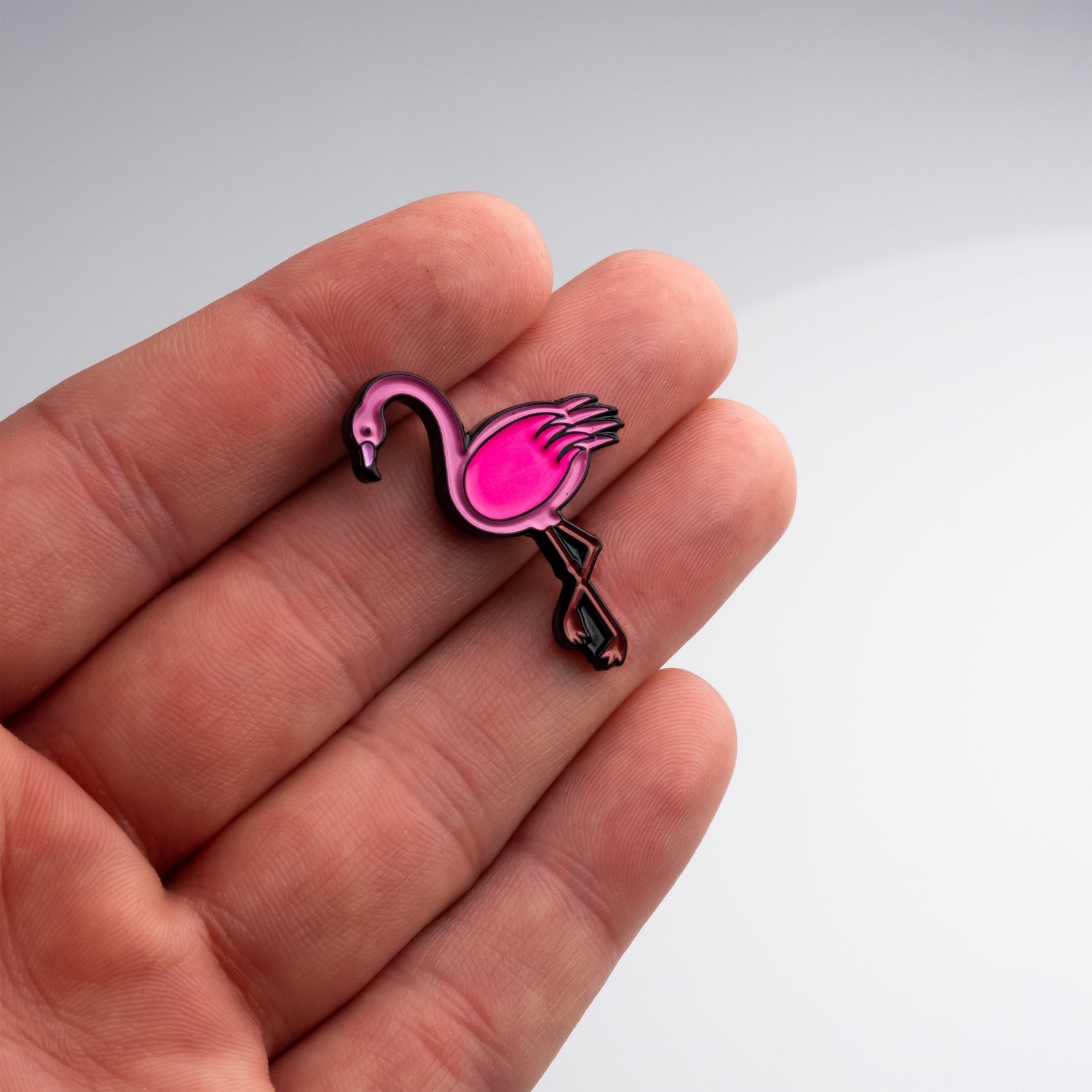 A hand holds the Pins and Aces Flamingo Ball Marker—a small, pink accessory ideal for magnetic surfaces—against a plain, light gray background.