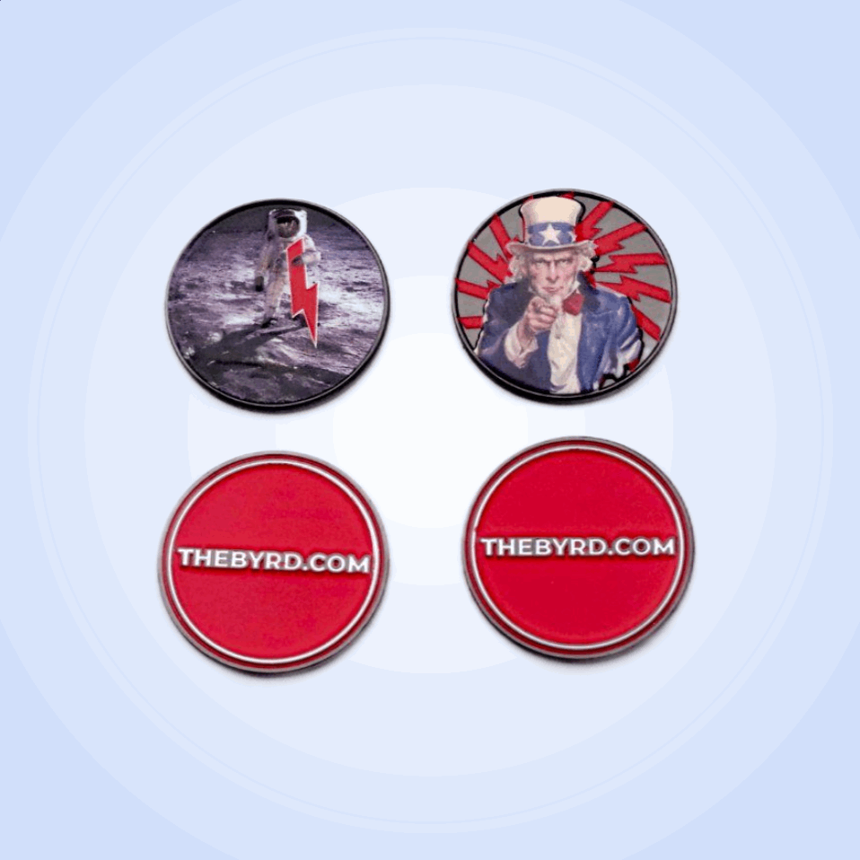 Four BYRD BALL MARKERS - Merica by The Byrd, LLC are arranged in a square: top left has an astronaut on the moon with a red lightning bolt, top right features Uncle Sam, and the bottom two are red with “THEBYRD.COM” in white text.