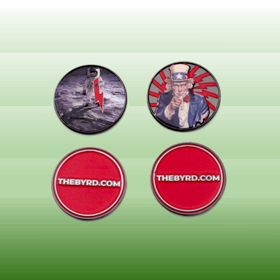 BYRD BALL MARKERS - Merica by The Byrd, LLC: Four round magnetic golf accessories—an astronaut with a red lightning bolt, an Uncle Sam design, and two reading THEBYRD.COM on red—stand out on a green gradient background.