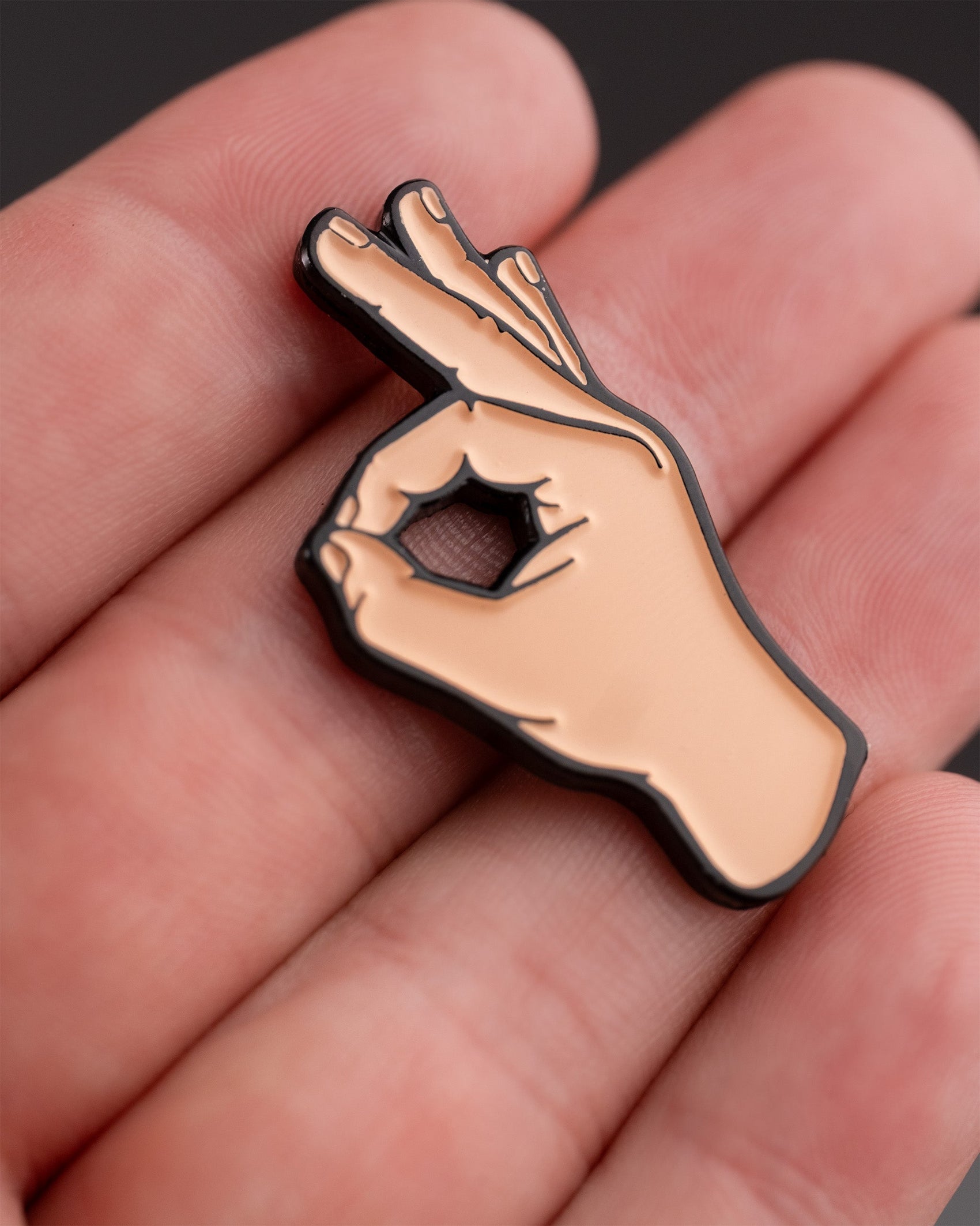 A close-up shows a hand holding the Pins and Aces OK Hand Ball Marker, an enamel golf marker shaped like a hand making the OK gesture—a unique premium accessory for golfers.