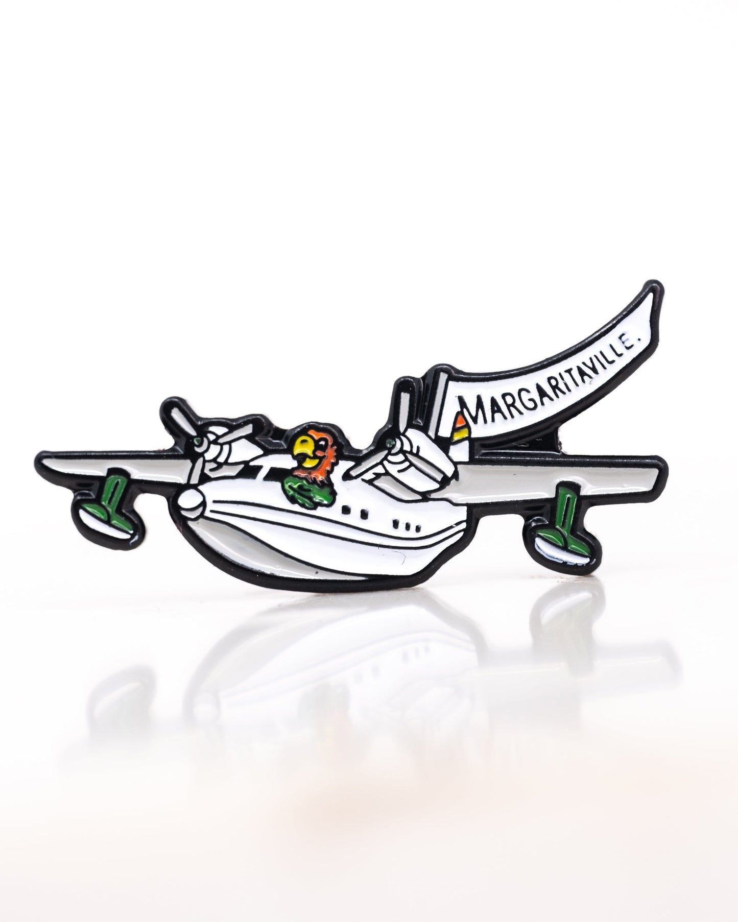 The Margaritaville Hemisphere Dancer Ball Marker by Pins and Aces features a cartoon seaplane with green wheels and a parrot pilot towing a white "MARGARITAVILLE" banner on a plain white background.