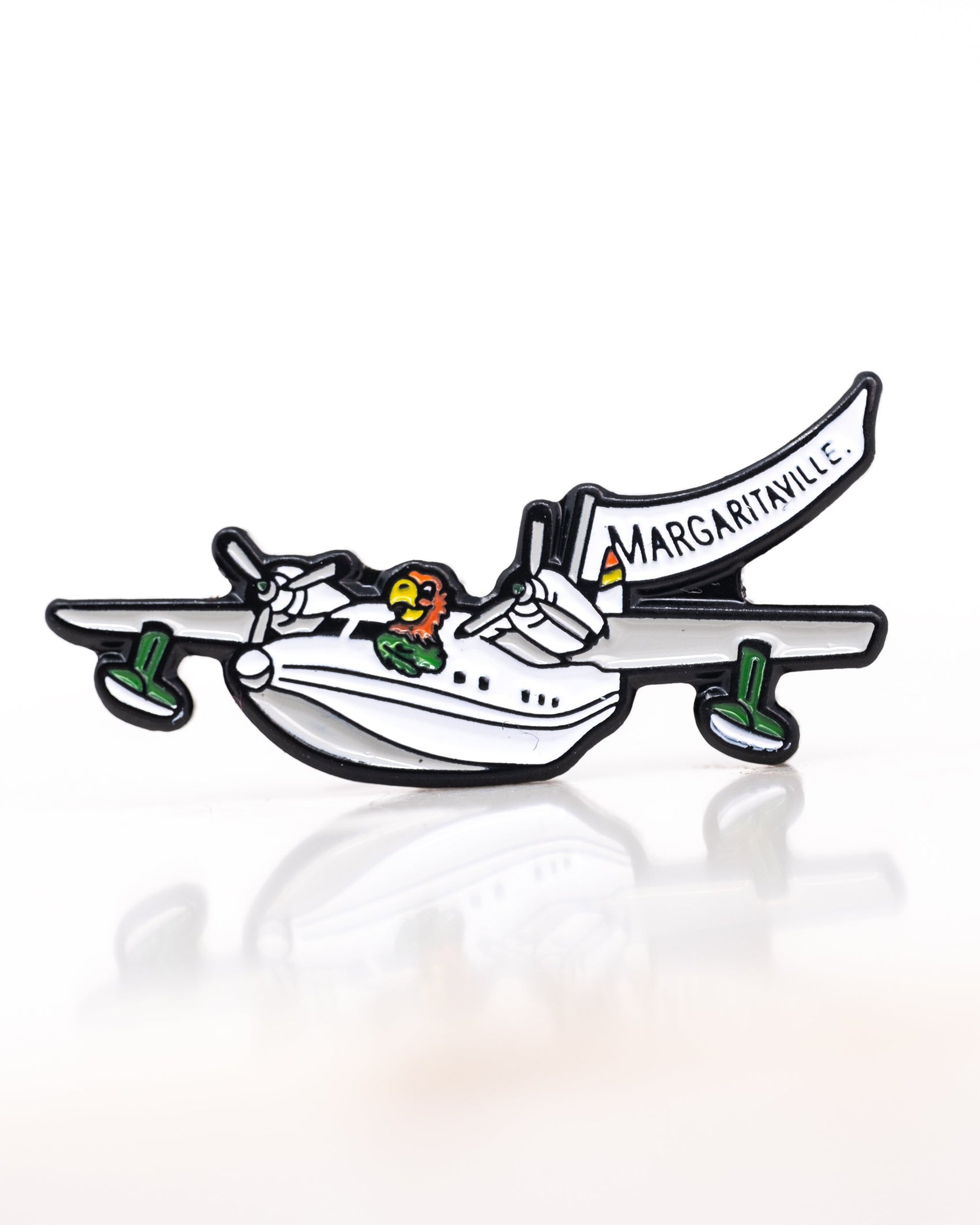 The Margaritaville Hemisphere Dancer Ball Marker by Pins and Aces features a cartoon seaplane with green wheels and a parrot pilot towing a white "MARGARITAVILLE" banner on a plain white background.