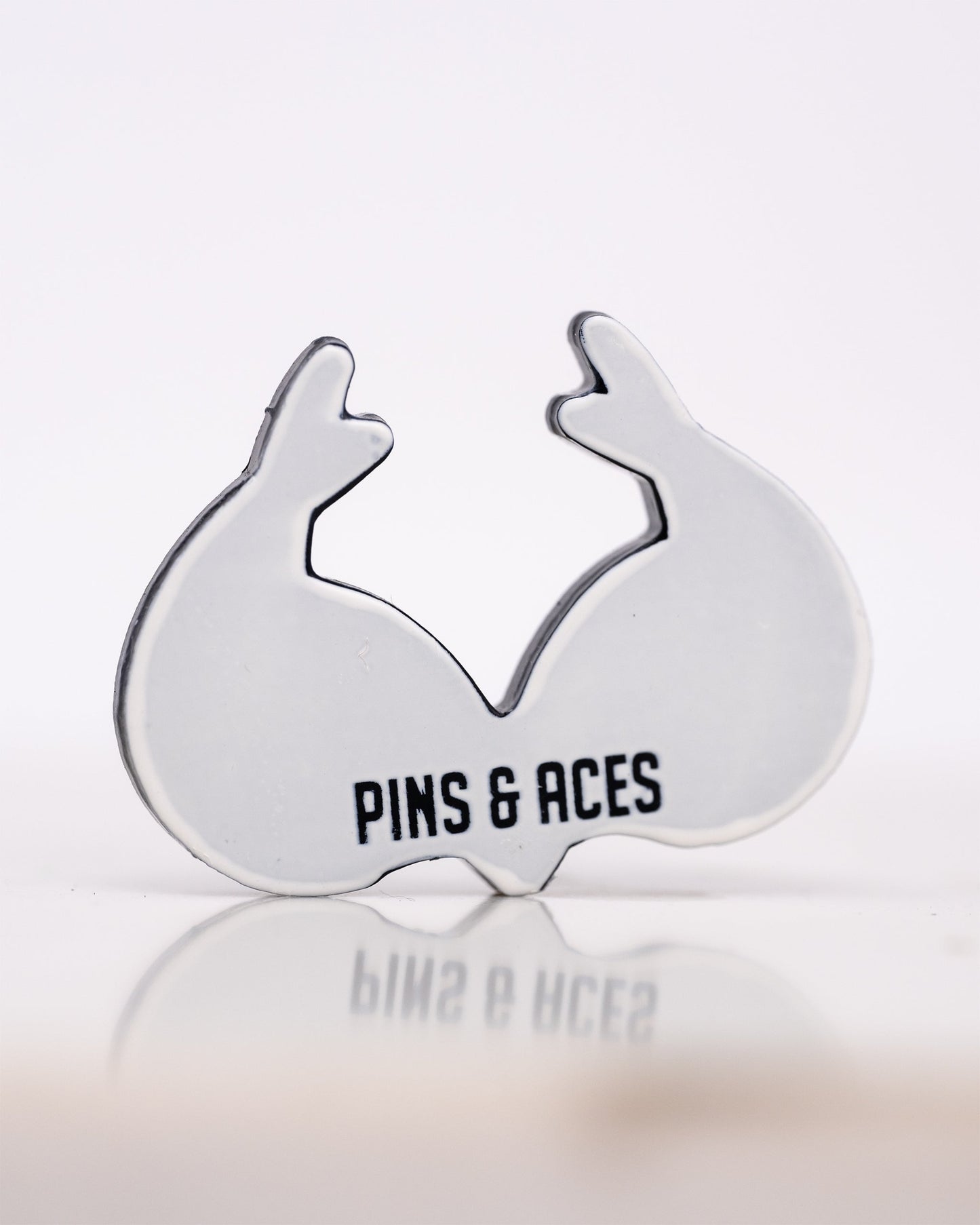 A ball marker shaped like real tree antlers with the text Pins and Aces printed on it, set against a plain white background.