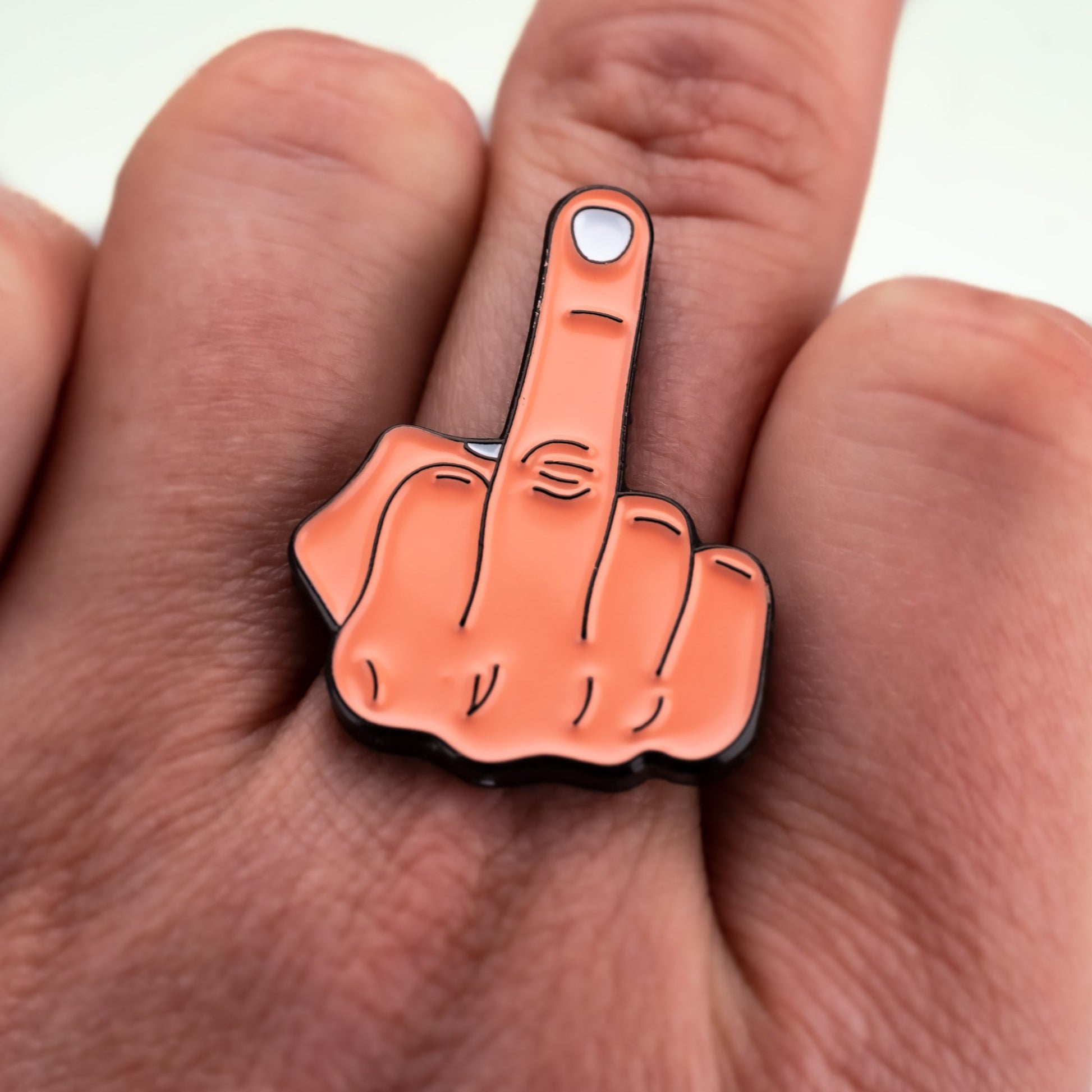 A close-up of a hand with the Middle Finger Ball Marker by Pins and Aces, an enamel pin shaped like a raised middle finger, featuring a magnetic surface for easy attachment to ball markers or stainless steel accessories.