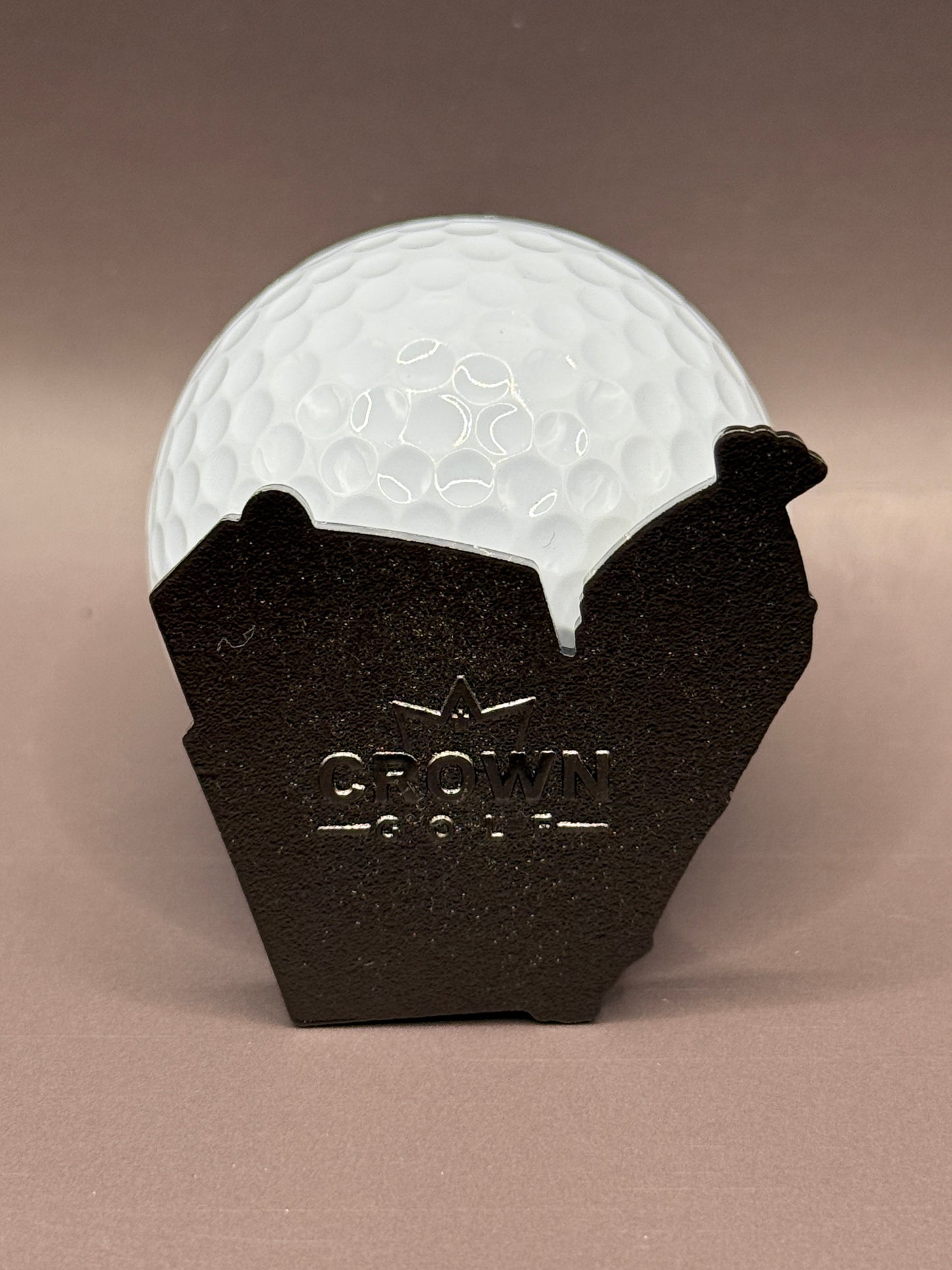A white golf ball rests in a magnetic black metal Arkansas-shaped holder engraved with "Best Buds Ball Marker" by Crown Golf Designs, set against a plain brown background.