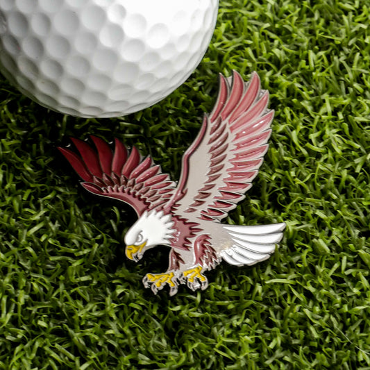 A golf ball rests on green grass beside the Bald Eagle Ball Marker by Ballmarkers.com—a striking metal pin shaped like a soaring eagle with spread wings and outstretched talons—making it a standout among patriotic golf accessories and perfect for golfers seeking a wildlife-inspired marker with distinctive flair.