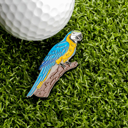 The Macaw Ball Marker by Ballmarkers.com—a vibrant nod to exotic birds—rests on artificial grass beside a pristine white golf ball, offering a playful and distinctive accessory for golfers seeking something unique.