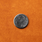 A round, black-and-gray marbled object—The Venom by Doubloon—is centered on a textured orange surface.