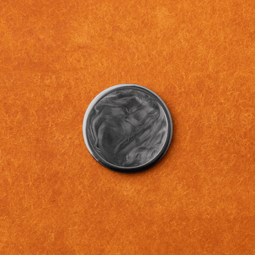 A round, black-and-gray marbled object—The Venom by Doubloon—is centered on a textured orange surface.