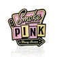 The Blazy Susan Smoke Pink Ball Marker by Pins and Aces features retro pink and yellow enamel text, "Smoke Pink," with "Blazy Susan" in cursive, and a stainless steel magnetic hat clip—ideal as a golf ball marker or accessory.