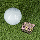 The Pins and Aces Blazy Susan Smoke Pink Ball Marker is a vibrant stainless steel accessory featuring "Smoke PINK, Think Urban," displayed alongside a white golf ball on bright green artificial grass.