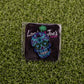 The Blue Sugar Skull ball marker by Logie Joe's Golf features vibrant blue, purple, and green hues on a black card with the palm tree logo—an artistic golf accessory that adds unique flair to your game.