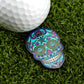 A vibrant Blue Sugar Skull ball marker by Logie Joe's Golf with intricate patterns rests on green grass beside a white golf ball, highlighting stylish, artistic golf accessories.