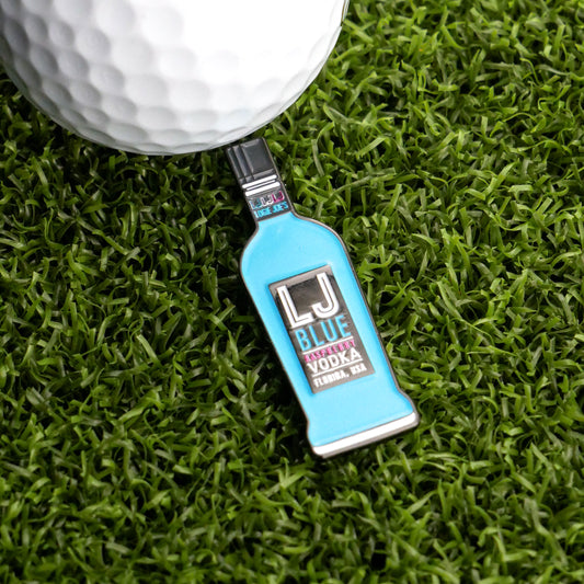 A Blue Vodka Ball Marker from Logie Joe's Golf, shaped like a bottle, rests on green artificial grass next to a white golf ball.